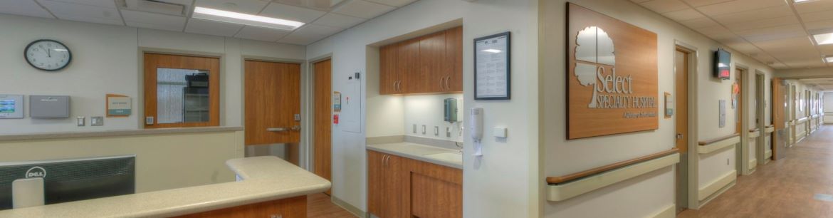 A view of Select Specialty Hospital Macomb including the nurses station, a hospital name sign and the hospital hallway.