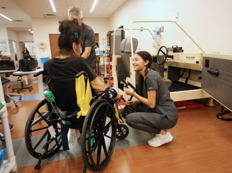 A patient in their wheelchair is helped to move into a model car used to learn to drive again after injury.