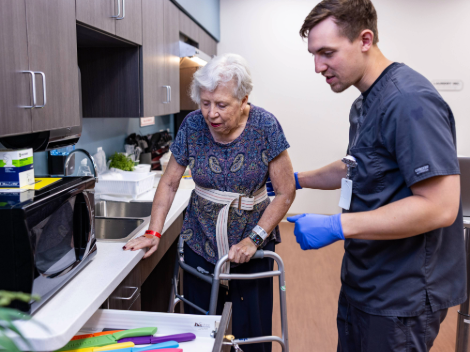 A patient stands in a kitchen working to cook alongside her therapist to relearn everyday life skills.