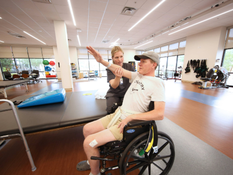A patient works on his range of motion in his arms with his therapist while sitting in his wheelchair.