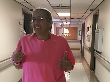 Edie in a hot pink t-shirt gives two thumbs outside her hospital room.
