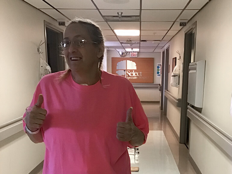 Edie in a hot pink t-shirt gives two thumbs outside her hospital room.