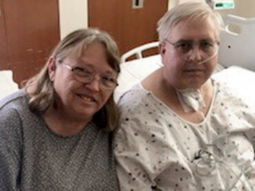 Gary's wife sits next to him in his hospital bed.