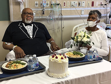Covid 19 survivor Glynn, now newlywed, holds hands with wife Edween in his hospital room before cutting the wedding cake.