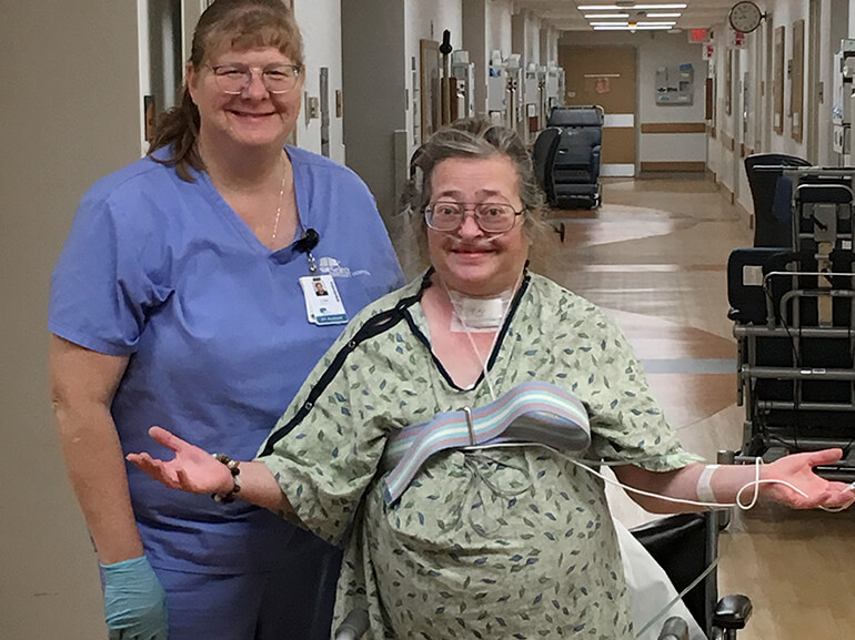 A smiling Lisa stands next to her occupational therapist in the hospital hallway.