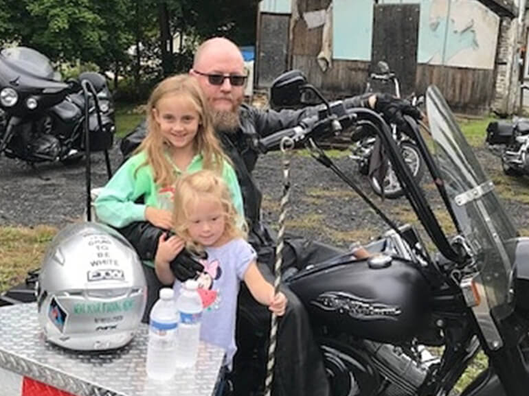 Michael sitting on his motorcycle posing with his two young daughters.