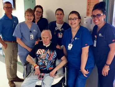 Ray, wearing a t-shirt of his favorite stock car driver Lance Dewease, sits in a chair surrounded by his care team.