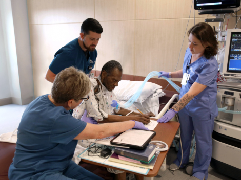 A patient sits on the edge of his hospital bed learning to write again and gain strength with the help of his care team.