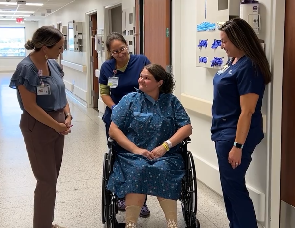 Women in leadership at Select Specialty Hospital - Tulsa talk with a patient in a wheelchair while standing in the hospital hallway.