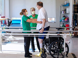 Two physical therapists assisting a patient on the parallel bars