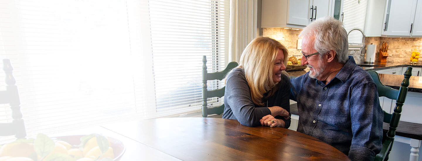 Smiling couple holding hands at a kitchen table, representing recovery and comfort.