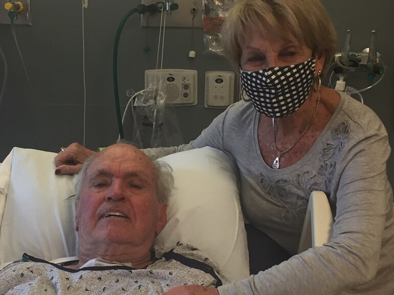 Bill Young laying in hospital bed with his wife beside him.