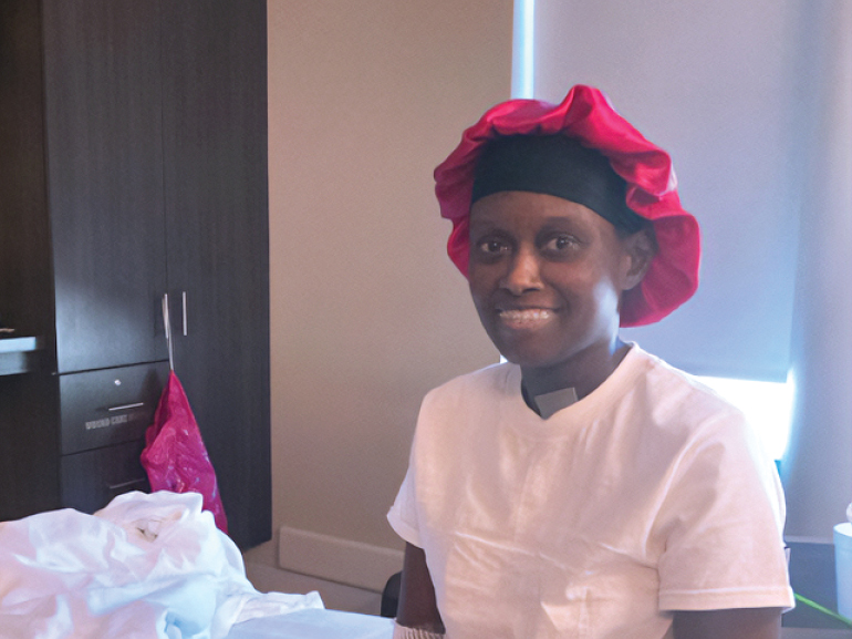 Jvonne in white shirt and pink cap smiles at the camera.