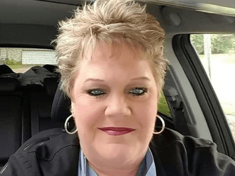 Stacie wearing hoop earrings and a dark top is seated inside a car, looking toward the camera.