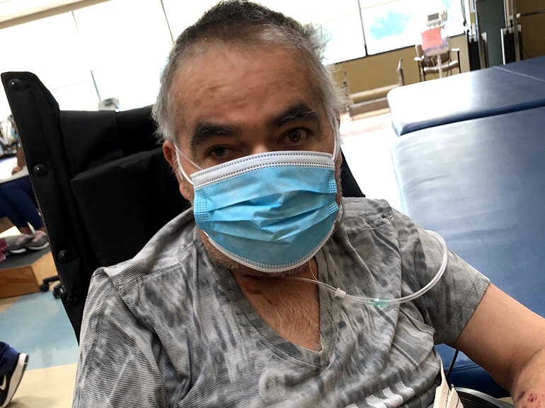 Jesus wearing a medical mask and sitting in a chair in a physical therapy room.