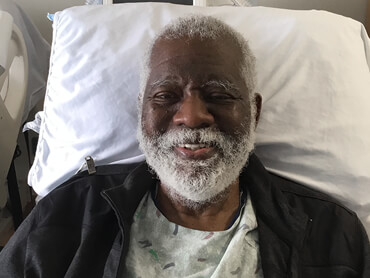 A smiling Lindsay sits up unassisted in his hospital bed.