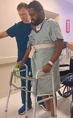 Laz walks down the hospital hallway with the help of his care team and a walker.
