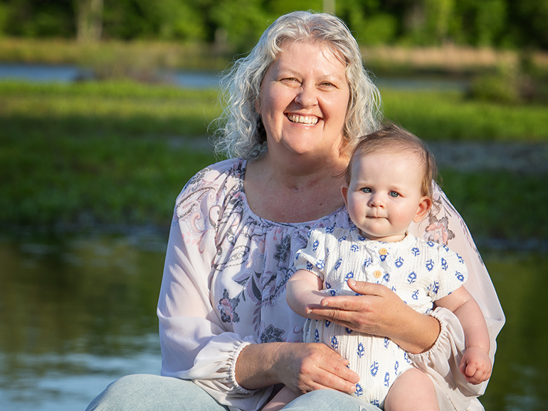 Angela Fawley, smiling and holding a baby in the yard outside a house.