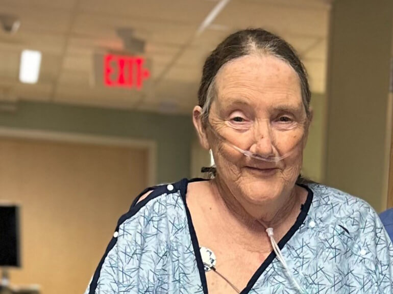 Close up of Loretta walking in the hallway at the hospital, wearing her hospital gown.
