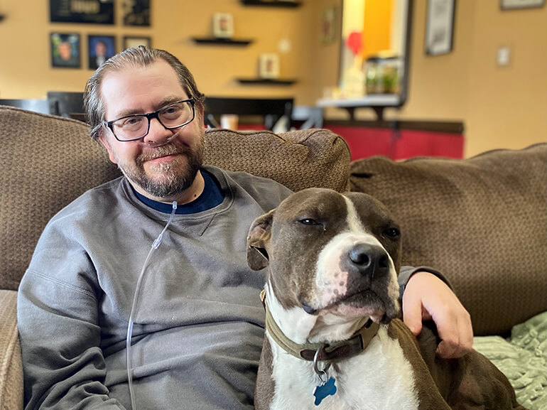 Mike Johnston, sitting on his couch, at home with his dog.