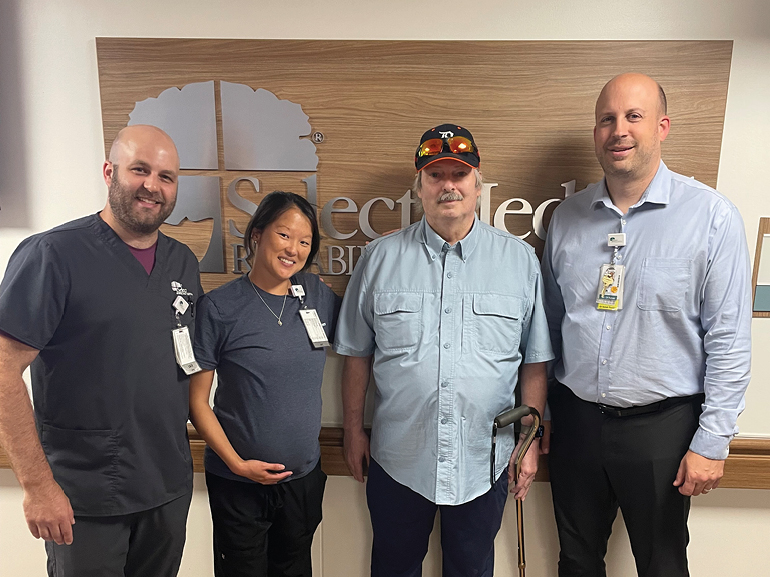 Steve and his care team pose for the camera in front of the hospital sign.